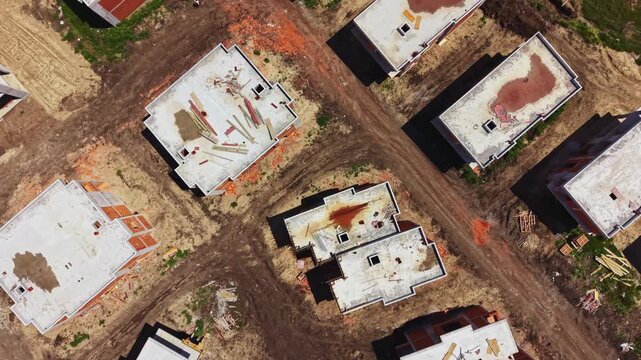 Bird s eye view shows several incomplete houses in a construction site. Dirt paths run between the buildings. Tools and materials are scattered around the area.