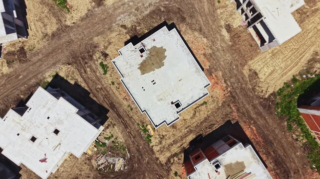 Workers are building new homes on empty land. There are several structures with concrete roofs and scattered materials. The scene shows active construction.