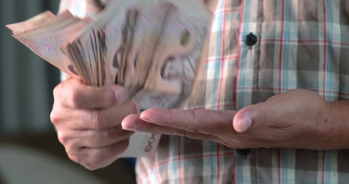 Man holding and slapping a stack of cash onto his palm, farmer holding money thai baht, finance, money, income, wealth, investment, and business economy concepts, close-up