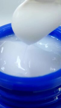 Mixing white moisturizing cream in blue tube with plastic spoon, close up view from front, skin care