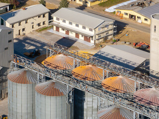 This aerial view shows silos and buildings in an industrial area during the day. A tractor is seen near the structures. © 24K-Production