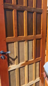 homem passando verniz pintando porta de madeira 
