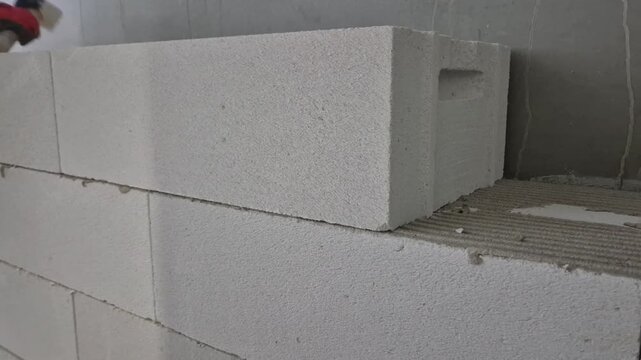 Building an aerated concrete block wall, front view, worker adjusting with a rubber mallet and checking with a spirit level, slow motion.
