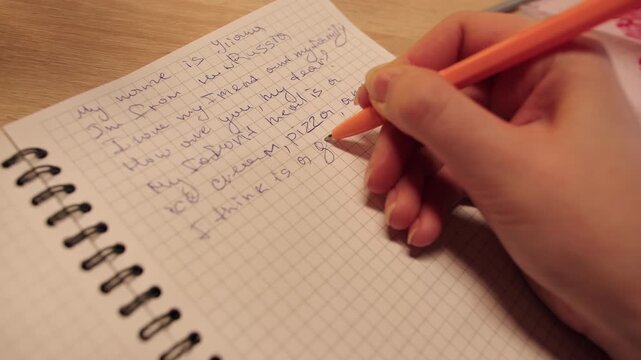 Focused caucasian woman carefully writes on grid paper with orange pen. Closeup of female hand that plans and arranges thoughts on structured grid paper in warm glow in evening living room