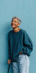 Obraz premium Older woman laughing while holding cane against blue wall