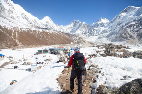 Adventurer trekking through snowy mountains with stunning peaks and clear blue sky backdrop. Nepal, Himalayas