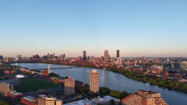Golden hour aerial drone view of the Boston skyline, featuring the Prudential and John Hancock towers rising above the historic Back Bay neighborhood and the calm waters of the Charles River.