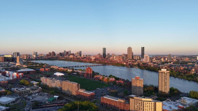 Golden hour aerial drone view of the Boston skyline, featuring the Prudential and John Hancock towers rising above the historic Back Bay neighborhood and the calm waters of the Charles River.