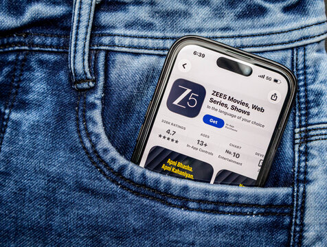Closeup of a smartphone screen displaying the zee5 mobile application store page, nestled inside the pocket of blue denim jeans