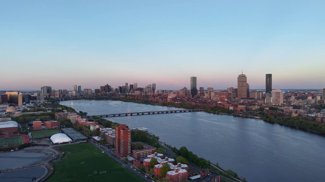 Golden hour aerial drone view of the Boston skyline, featuring the Prudential and John Hancock towers rising above the historic Back Bay neighborhood and the calm waters of the Charles River.