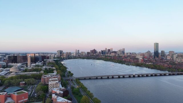 Golden hour aerial drone view of the Boston skyline, featuring the Prudential and John Hancock towers rising above the historic Back Bay neighborhood and the calm waters of the Charles River.
