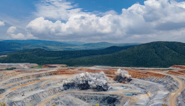 Explosive works on open pit gold mine industry with dust and puffs of smoke.