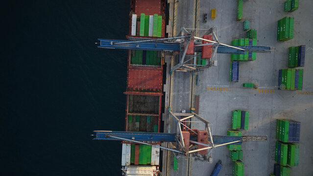 Mercante en muelle de carga junto a gr&uacute;a y camines cargando contenedores en el barco , vista a&eacute;rea cenital