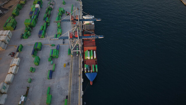 Mercante en muelle de carga junto a gr&uacute;a y camines cargando contenedores en el barco , vista a&eacute;rea cenital