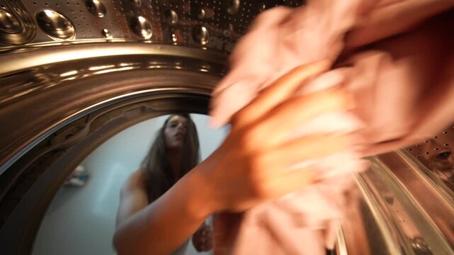 Woman sorts and arranges clothes in washing machine at home