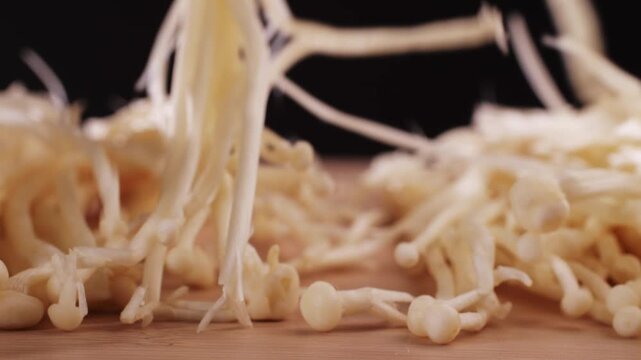 Fresh golden needle mushroom or enoki, enokitake (Flammulina velutipes) on wooden plate, close up macro of vegan food.