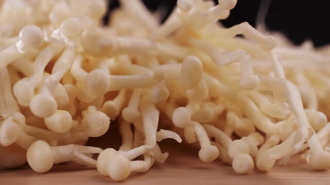 Fresh golden needle mushroom or enoki, enokitake (Flammulina velutipes) on wooden plate, close up macro of vegan food.