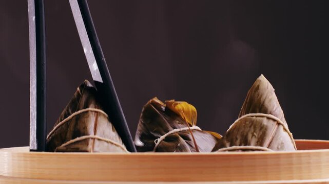 Hand holding zongzi (rice dumpling) with savoury fillings wrapped in bamboo or reed leaves.