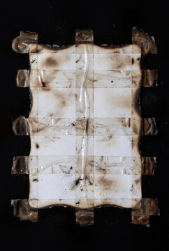 Abstract burned paper texture composed of scorched white sheets arranged in a geometric grid on a dark black background.