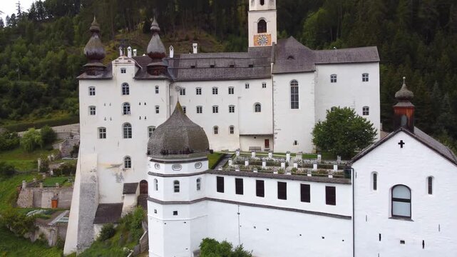 4K aerial view of Marienberg Abbey, Europe's highest Benedictine monastery in South Tyrol, Italy. Scenic white baroque basilica surrounded by alpine mountains and lush green vineyards in summer.