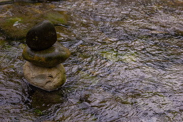 Close-up of a small stack of balanced zen stones standing in the shallow water of a flowing stream. Concept of inner peace, stability, and mindfulness.