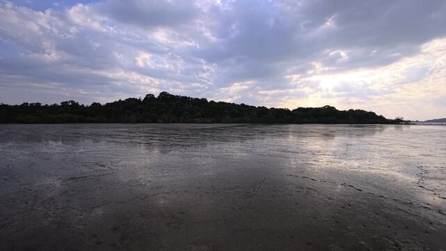Low tide mudflat with sun rays breaking through clouds over coastline