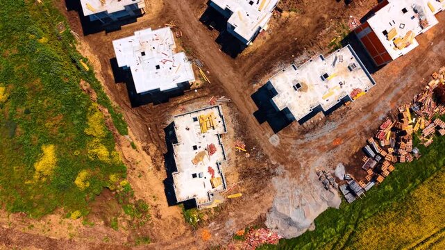 Top down aerial view of cottage construction site and materials. Straight down drone shot of concrete house structures under construction with bricks.