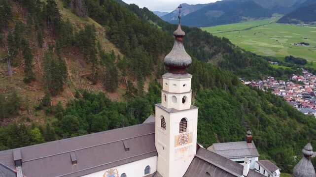 4K aerial view of Marienberg Abbey, Europe's highest Benedictine monastery in South Tyrol, Italy. Scenic white baroque basilica surrounded by alpine mountains and lush green vineyards in summer.