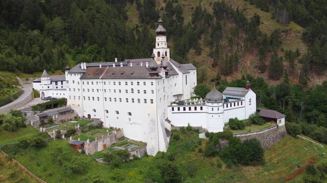 4K aerial view of Marienberg Abbey, Europe's highest Benedictine monastery in South Tyrol, Italy. Scenic white baroque basilica surrounded by alpine mountains and lush green vineyards in summer.