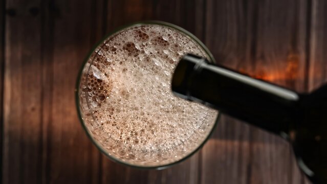A bottle pouring beer into a glass, creating bubbles, viewed from above. Concept of refreshment, advertising content for bars, pub, cafes, and restaurants, celebration, nightlife and social gatherings
