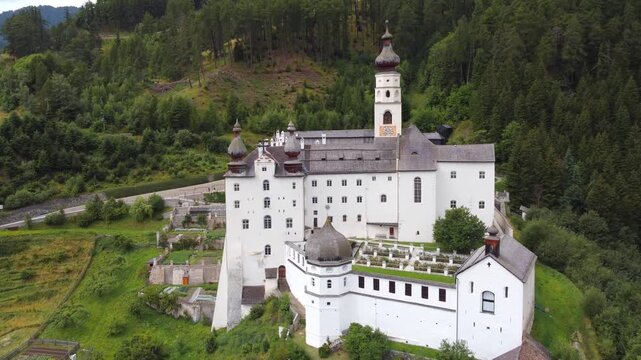 4K aerial view of Marienberg Abbey, Europe's highest Benedictine monastery in South Tyrol, Italy. Scenic white baroque basilica surrounded by alpine mountains and lush green vineyards in summer.