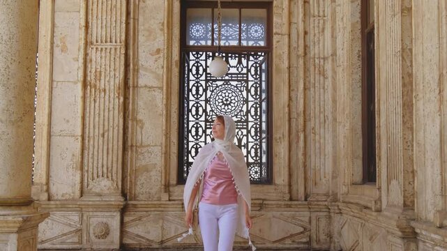 Slow motion shot of female traveler walking toward camera inside historic mosque corridor in Cairo, Egypt. Elegant Islamic architecture and ornate marble details in cinematic 4K travel footage.