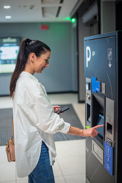 Woman making contactless paying at parking payment machine in the parking garage
