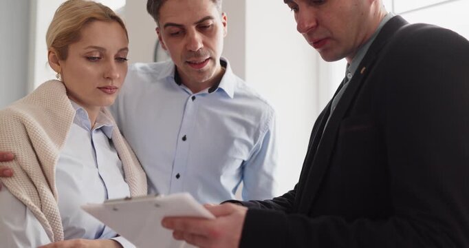 Couple and agent in contract discussion. Clients review documents with a realtor in an apartment, weighing rent versus purchase and clarifying fees and timeline. Clear home deal choice concept.