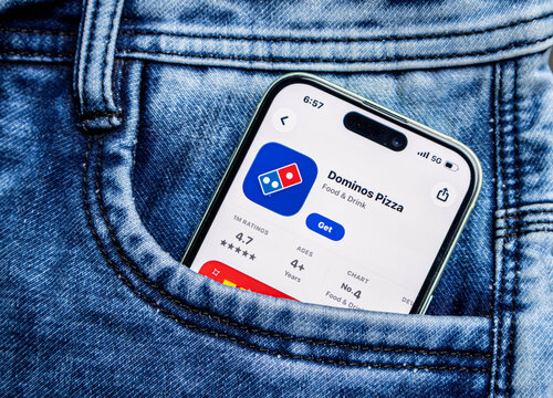 Smartphone in a blue denim jeans pocket displaying the dominos pizza app store page on the screen