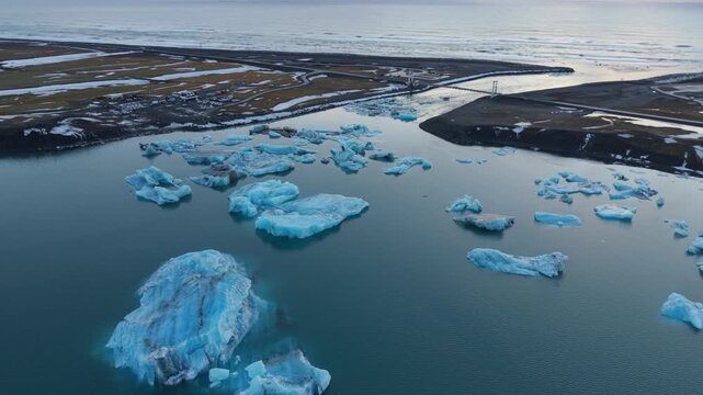 Aerial view of Jokulsarlon Glacier Lagoon with blue icebergs floating in the water near the bridge and dark volcanic sand in Sveitarfelagid Hornafjordur, Iceland.