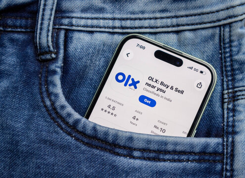 Smartphone showing the olx india app store page inside a blue denim jeans pocket, closeup view of mobile screen displaying classifieds app