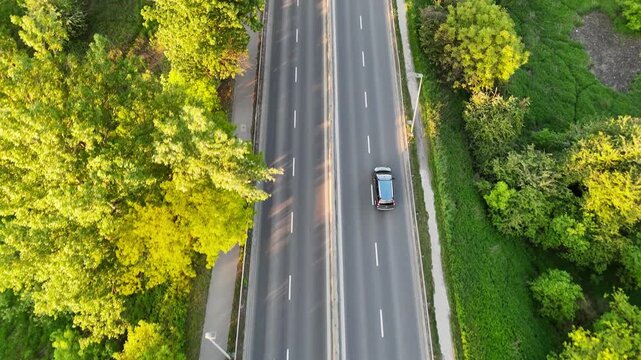 Aerial view of vehicles traveling on a multi-lane road surrounded by lush greenery, showcasing the flow of traffic and the vibrant landscape in the background. Cars riding at rural route
