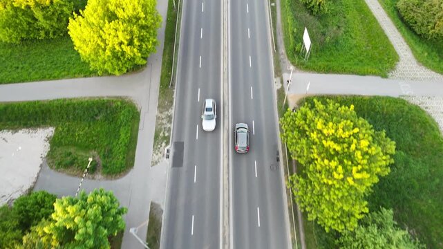 Aerial view of vehicles traveling along a tree-lined road, showcasing the continuous flow of traffic amidst lush greenery and urban elements in a suburban setting. Cars riding at rural route