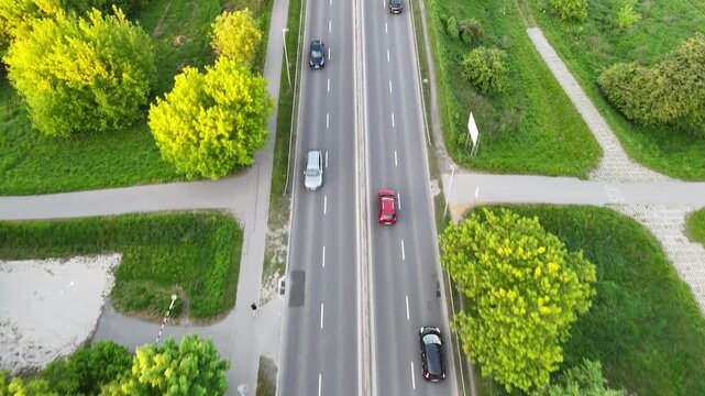 Aerial view of vehicles traveling on a multi-lane road surrounded by lush greenery, showcasing the flow of traffic and the vibrant landscape in the background. Cars riding at rural route