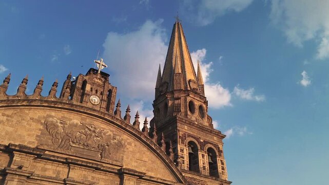 Guadalajara Cathedral close up main facade featuring the historic clock cross and twin towers is captured in a cinematic aerial drone tilt up orbit movement during a beautiful sunset.