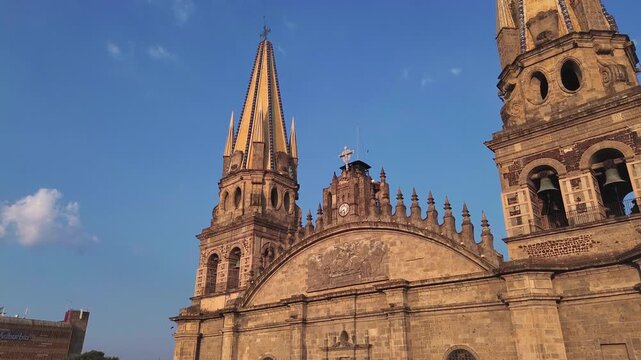 Guadalajara Cathedral close up main facade featuring the historic clock cross and twin towers is captured in a cinematic aerial drone tilt up orbit movement during a beautiful sunset.