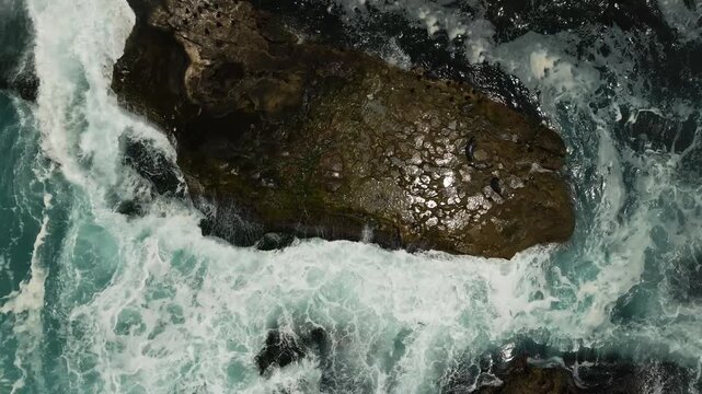 Aerial view of sea lions resting on a rocky outcrop with crashing waves and white foam at La Jolla Cove, San Diego, California, United States.