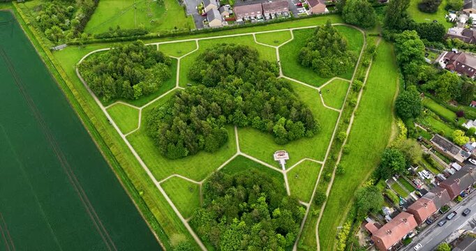 Aerial drone footage of geometric woodland park and crop fields beside residential housing in Selby North Yorkshire UK during spring with organised pathways and green landscape