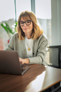 Middle-aged female professional working on a laptop in a bright modern corporate office