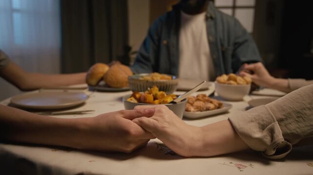 Close up shot of loving religious family clasping hands and saying prayer at dinner table in cozy home setting, copy space