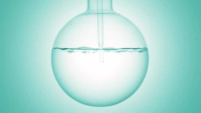 Close-up shot of pale cyan transparent liquid injected through a long dropper into a round-bottom flask, causing swirls and bubbles on cyan ramp background