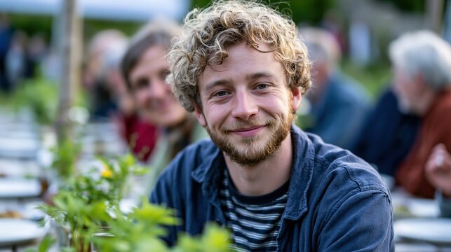 Young man smiling at outdoor community meal with family and neighbors