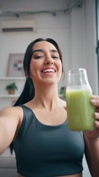 Video of itness woman drinking a healthy green juice while taking a selfie with smartphone in the kitchen at home
