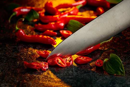 Kitchen knife and ​​​​wedges of red hot chili peppers on a kitchen table.